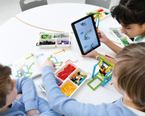 Dzieci ukłądają model z lego education na białym stole. Mają instrukcję otwartą na tablecie.