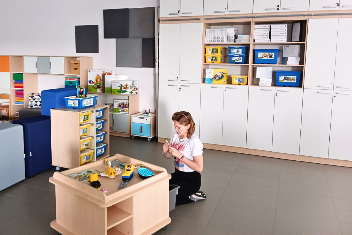 show room lego w firmie moje bambino, duże pomieszczenie z meblami, na których stoją zestawy lego w pudełkach, dziewczyna na podłodze skłąda model z lego przy stoliku