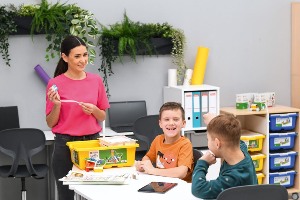 Nauczycielka pokazuje silnik z zestawu lego education uczniom, chłopcy śmieją się, są zaangażowani. Realizują steamowy projekt.